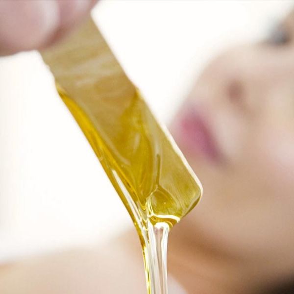 Blurred image of female spa client looking at hot wax on stick