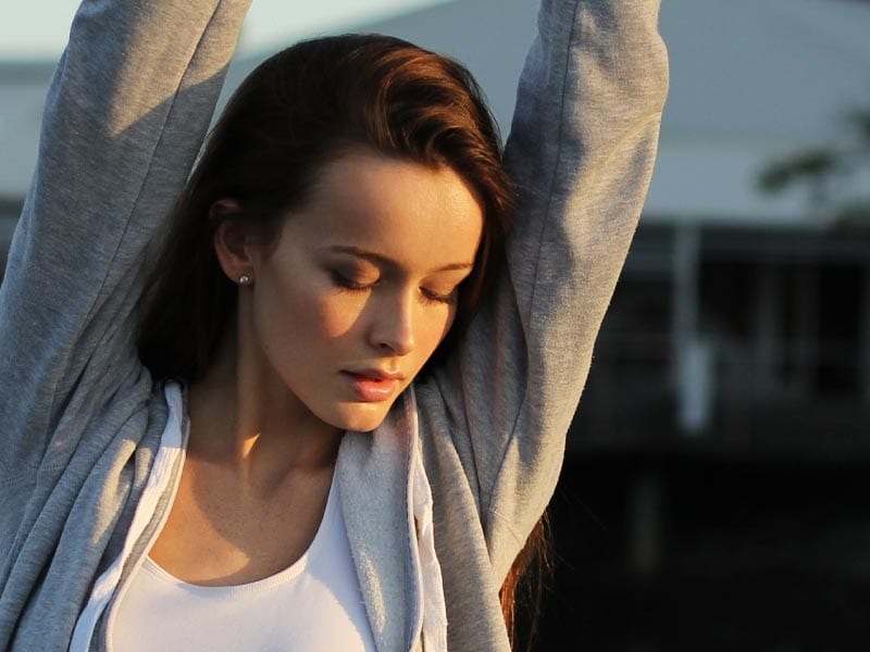 female model stretches arms over her head with her eyes closed