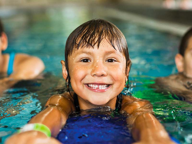 three cute children swim in the Zenergy pool during a youth swimming class
