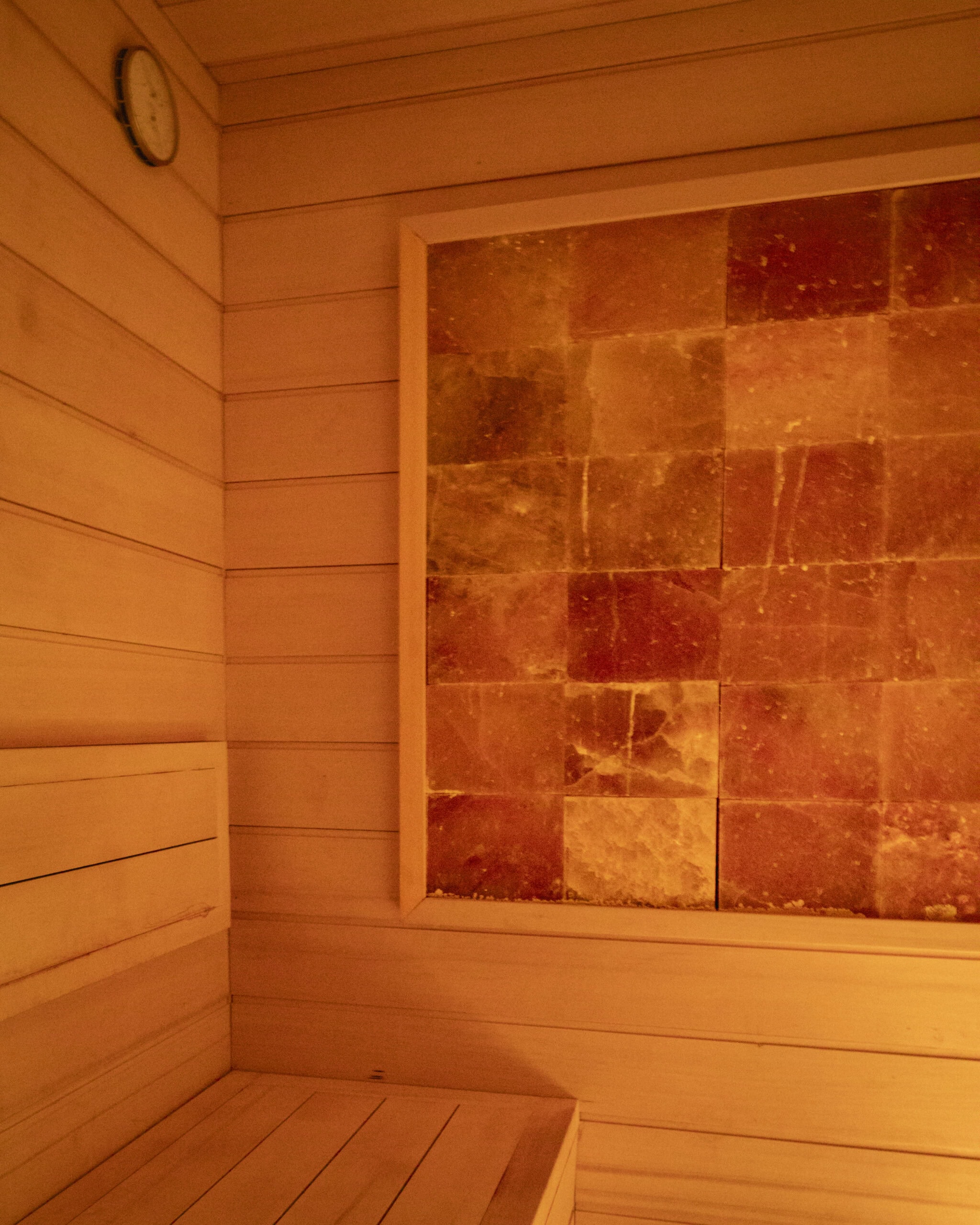 Wood-paneled sauna interior with a wall clock and a framed section of orange and yellow salt blocks, offering a tranquil retreat reminiscent of a Sun Valley spa or health club experience.